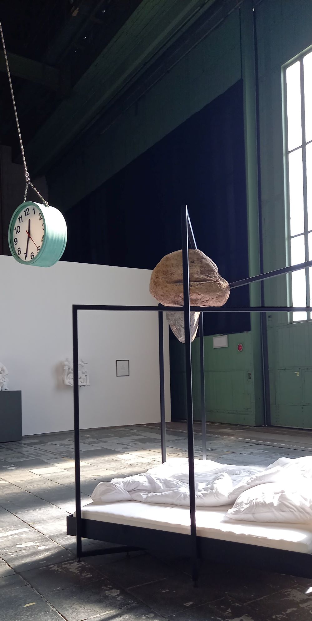 schwingende Uhr über Metallbett - Installation der polnisch deutschen Künstlerin Alicja Kwade