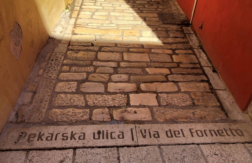 Kopfsteinpflaster mit zweisprachiger Inschrift "Pekarska ulica, via del Fornetto"